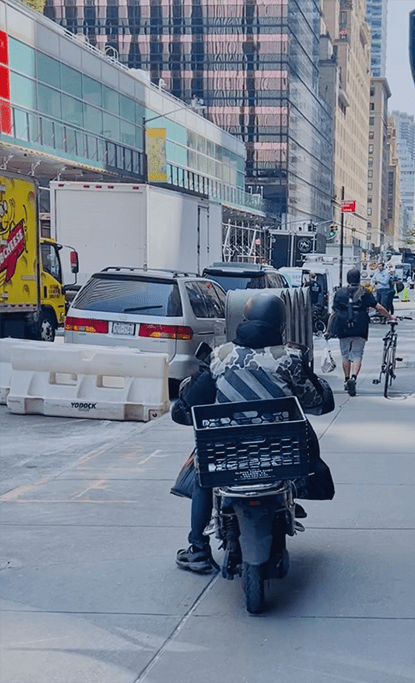 A moped operator driving on the sidewalk in New York City.